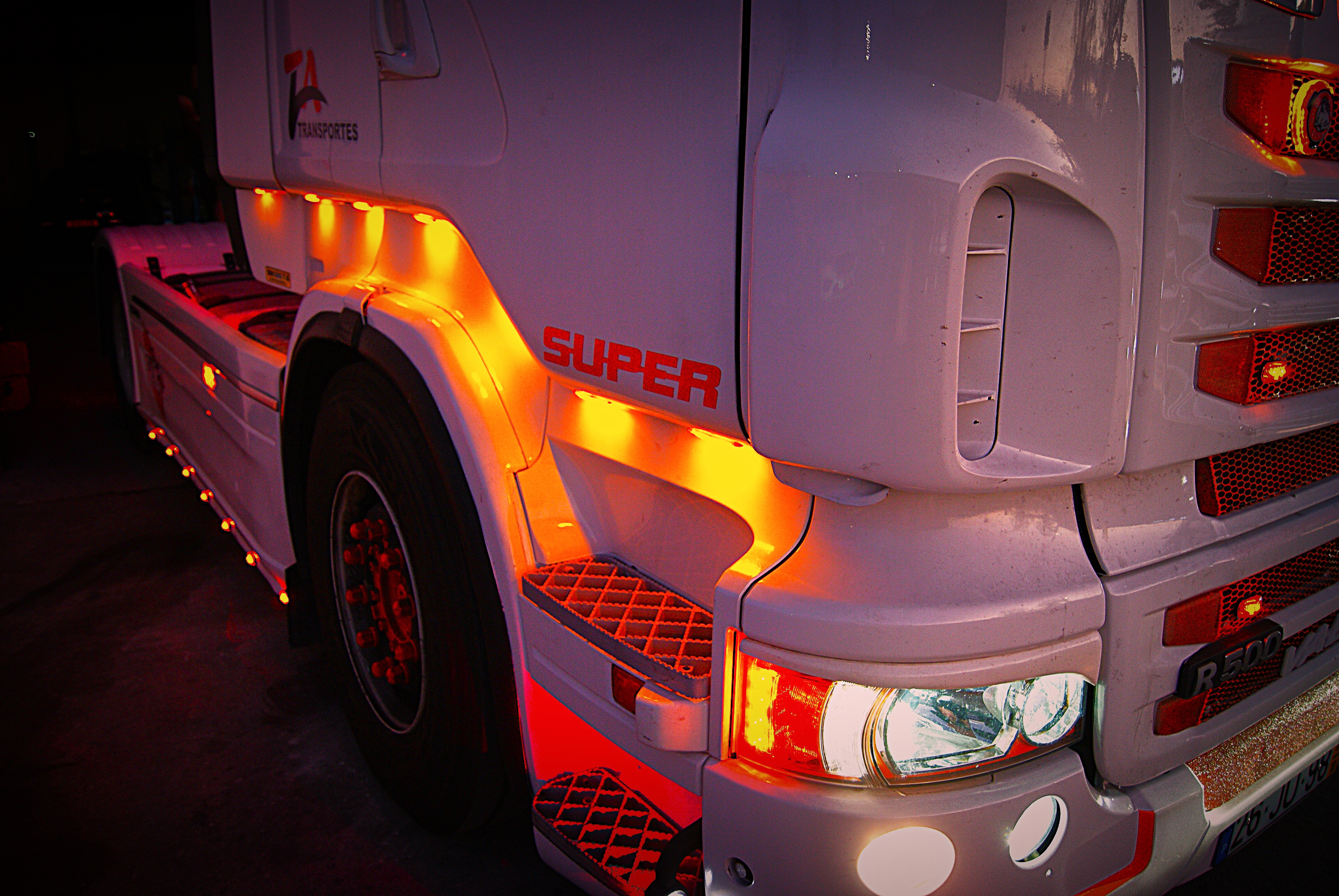 Imagem próxima da lateral de um camião, mais especificamente dos degraus por baixo da porta com as luzes acesas.
