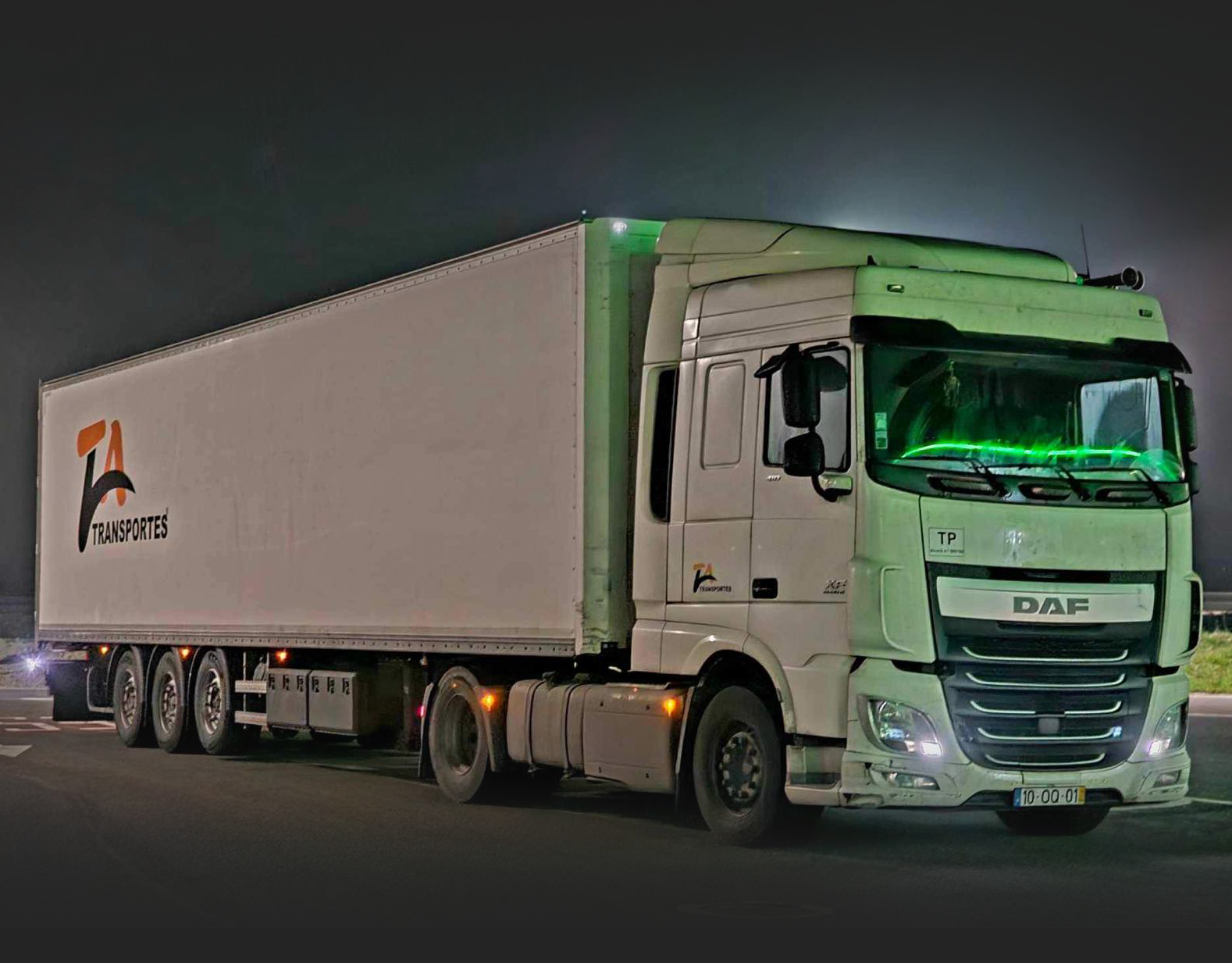 Imagem do serviço ibérico, um camião branco de frente na estrada de noite com reflexos de luzes verdes com o logotipo da Ta Transportes na laateral