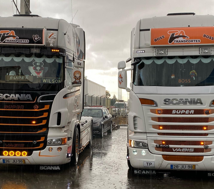 Imagem de dois camiões da TA Transportes lado a lado à chuva.